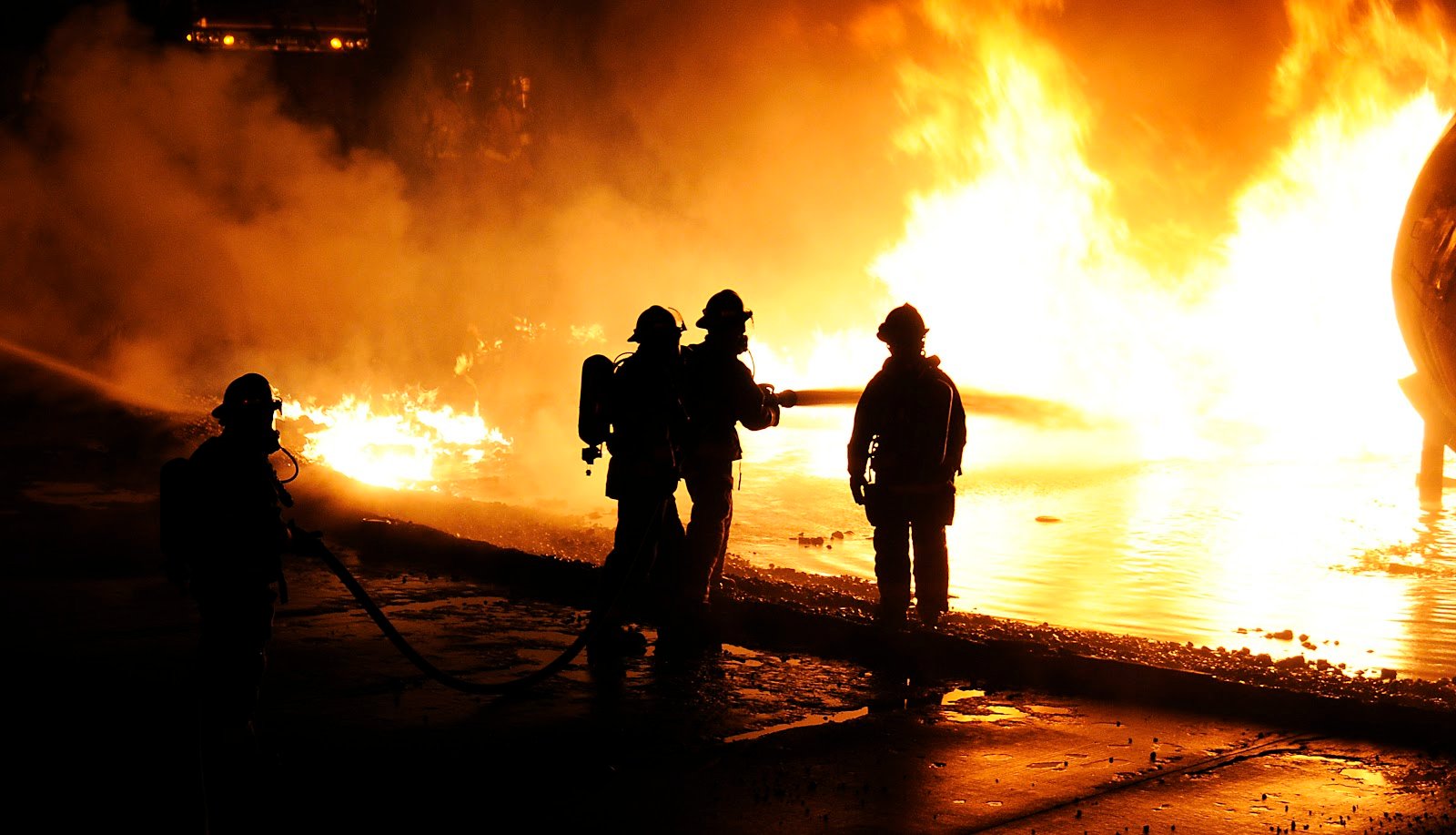 Firefighters using fire hose to reduce flames from a fire